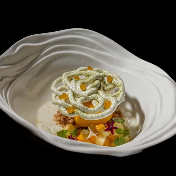 Artistic mango dessert with cream, fruit, and herbs in a modern white bowl