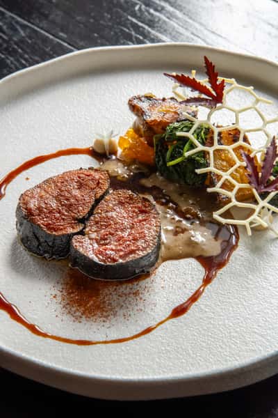 Gourmet meat dish with vegetables and artistic plating on a white plate