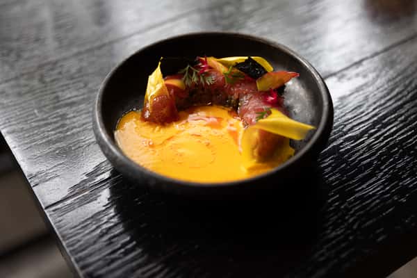 Gourmet seafood dish with yellow sauce, sliced fish, delicate herbs, and colorful garnishes.