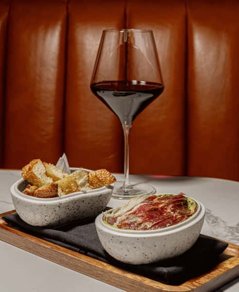 Cured ham tapas served with toasted bread and a glass of red wine.