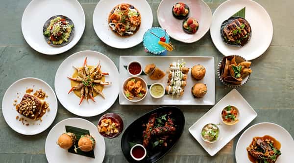 Assortment of appetizers and small plates, including tacos, seafood, pastries, and a blue cocktail.