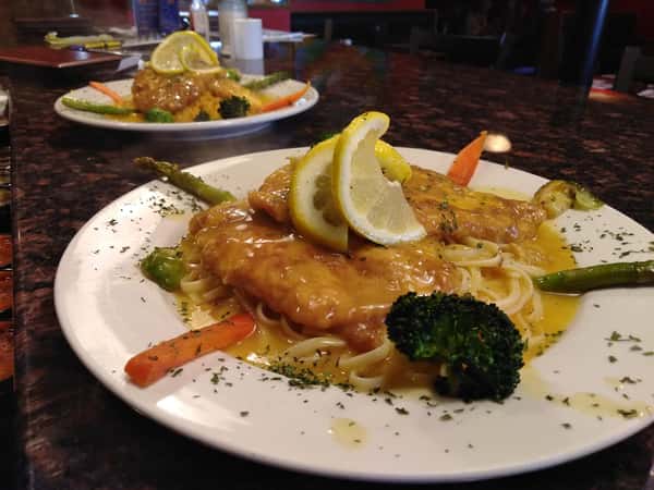 Chicken Francaise with pasta and sauteed vegetables and a lemon wedge