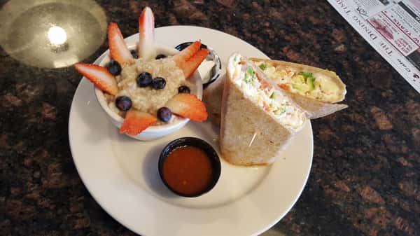 breakfast wrap with eggs and a fruit cup on the side.