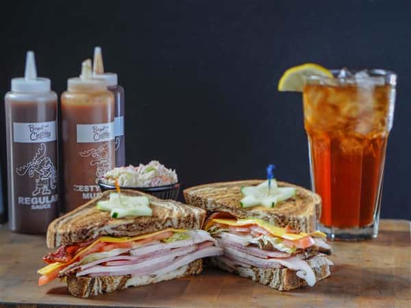 Sandwich served with sauces and side salad, with a glass of iced tea
