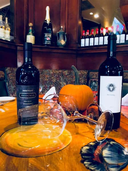two wine bottles on a table with wine glasses and pumpkin decorations