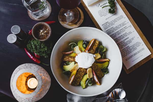 Overhead view of a beautifully plated gourmet dish featuring colorful roasted vegetables, fresh herbs, and a creamy white sauce, served in a ceramic bowl on a dark restaurant table.