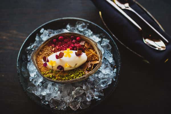 Elegant plated dessert featuring a delicate pastry topped with cream, fresh berries, edible flowers, and colorful garnishes, served on a dark textured plate.