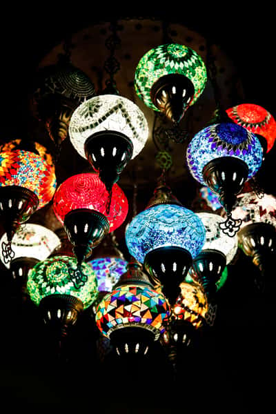 A stunning array of colorful mosaic lanterns hanging from a ceiling, featuring intricate designs in vibrant hues of red, blue, green, and yellow, creating a warm, inviting atmosphere.
