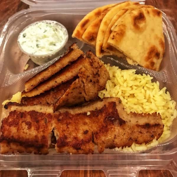 Gyro meat served with yellow rice, warm pita slices, and a side of creamy tzatziki sauce in a takeout container.