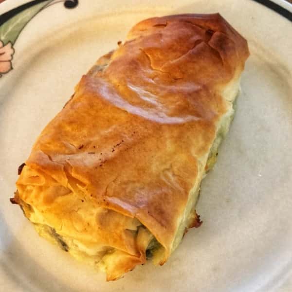 Golden-brown spanakopita with flaky phyllo dough, filled with spinach and feta cheese, served on a decorative plate.