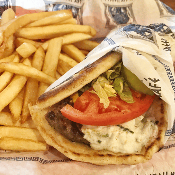 Beef gyro wrap with tomato, lettuce, pickles, and tzatziki sauce, served with a side of golden French fries.
