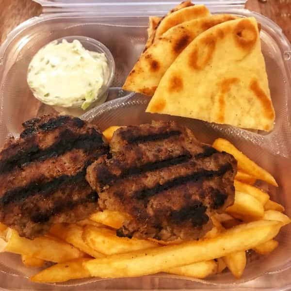 Grilled beef patties served with French fries, warm pita slices, and a side of tzatziki sauce in a takeout container.