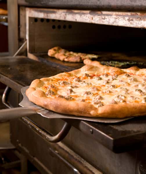 A pizza pie being removed from the oven