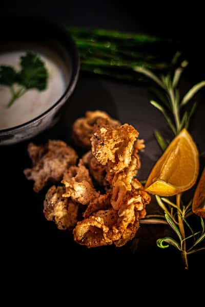 Crispy fried calamari served with lemon wedges, fresh rosemary, and a bowl of creamy dipping sauce garnished with parsley.