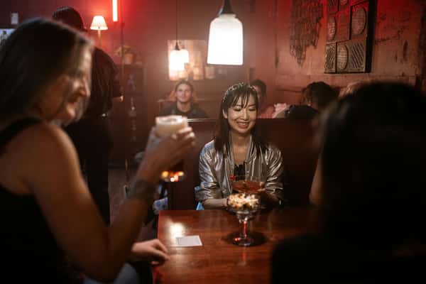 Friends enjoying drinks in a dimly lit bar with red neon accents.