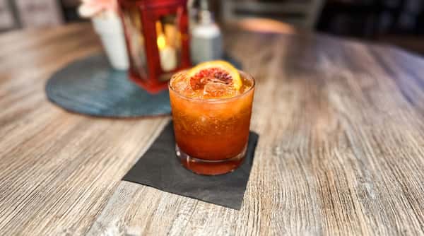 Cocktail with ice and a blood orange slice on a black napkin, on a wooden table with a red lantern in the background.