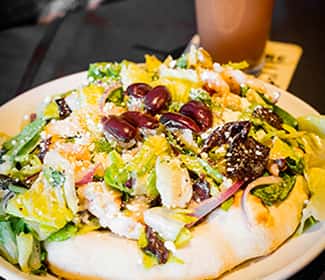 Fresh mixed greens salad topped with grapes, orange slices, feta cheese, and a light vinaigrette, served on warm flatbread for a vibrant and refreshing dish.