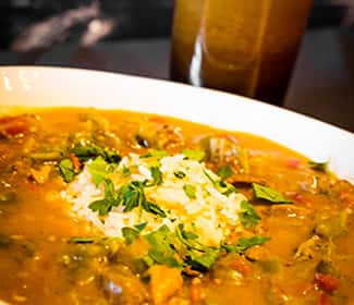 A hearty bowl of gumbo-style stew topped with a scoop of white rice and fresh chopped parsley, served in a rich, savory broth with vegetables and spices.
