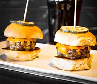 Juicy beef sliders topped with melted cheddar cheese and garnished with pickle slices, served on soft toasted buns for a classic appetizer or snack.