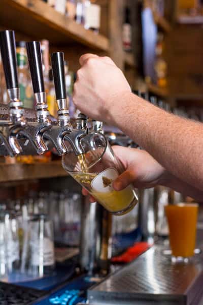 Bartender pouring a fresh draft beer from a tap behind the bar.