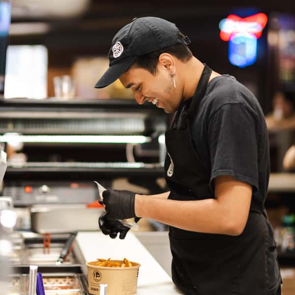 Friendly staff member preparing a fresh order of fries inside The Spoke café and bar kitchen.