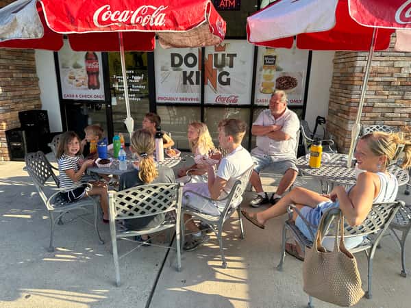 Children enjoying donuts outside Donut King under Coca-Cola umbrellas.