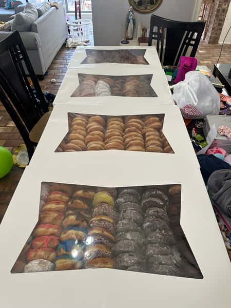 Four large bakery boxes filled with assorted donuts placed on a long dining table inside a home