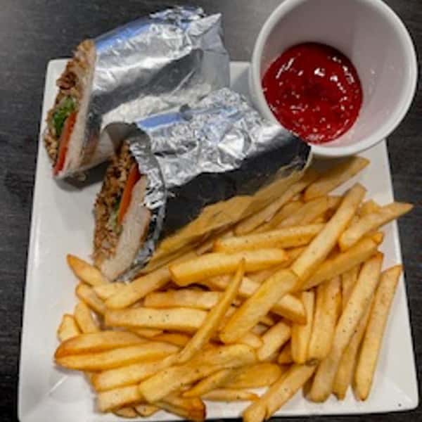 Grilled chicken sandwich wrapped in foil, served with crispy French fries and a side of ketchup on a square white plate.