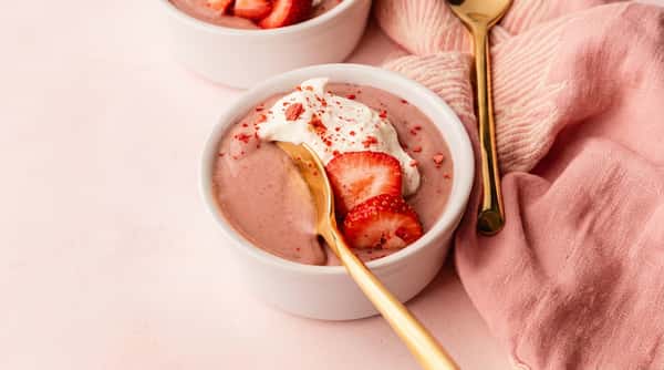 Strawberry mousse or yogurt with whipped cream and sliced strawberries in a white bowl, a golden spoon resting inside.