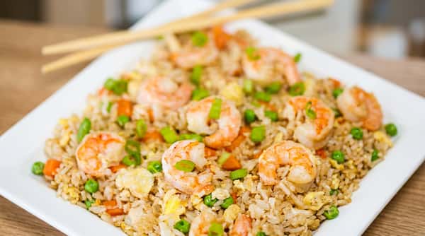 Shrimp fried rice with peas, carrots, scrambled egg, and chopped green onions, with chopsticks.