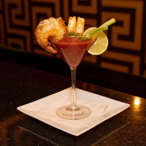Shrimp cocktail served in a martini glass with cocktail sauce, garnished with lime, celery, and herbs.