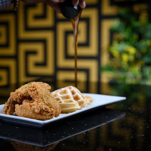 Fried chicken and waffles on a plate with syrup being poured on top.