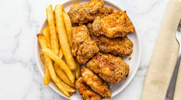Crispy breaded chicken nuggets with golden french fries on a white plate.