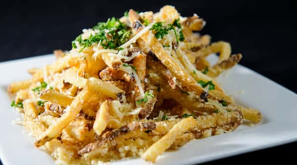 Garlic Parmesan fries topped with shredded cheese and chopped green herbs on a white plate.