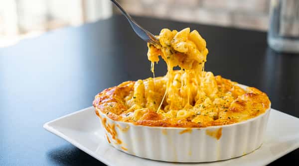Macaroni and cheese in a white ramekin, with a fork lifting a cheesy serving.