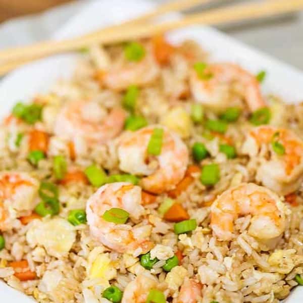 Shrimp fried rice with peas, carrots, and scrambled eggs, garnished with chopped green onions on a white plate.