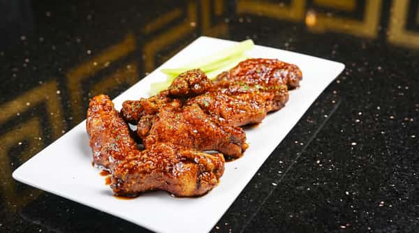 Sticky glazed chicken wings with celery sticks on a white rectangular plate.