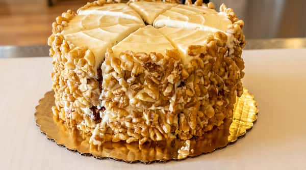 Sliced carrot cake with white cream cheese frosting and walnuts covering the top and sides.
