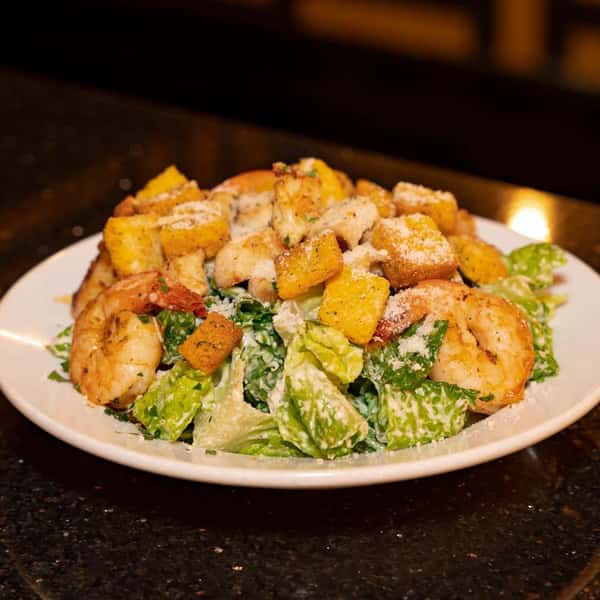 Caesar salad topped with grilled shrimp, golden croutons, and grated parmesan cheese on a white plate.
