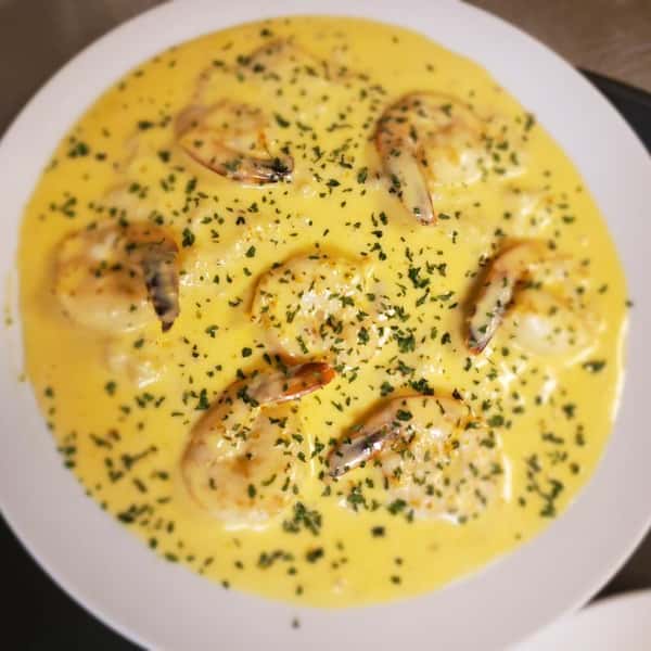 Shrimp covered in a creamy yellow sauce, garnished with chopped herbs, served on a white plate.
