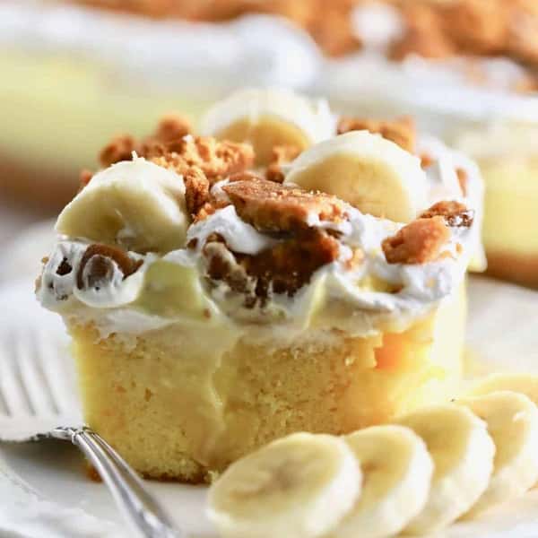 Banana pudding cake topped with whipped cream, banana slices, and crushed cookies.