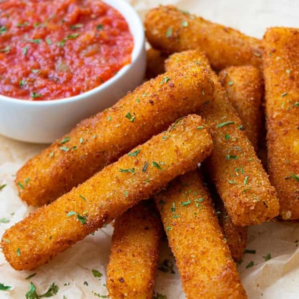 A close-up of crispy breaded mozzarella sticks garnished with parsley, served with a bowl of rich marinara dipping sauce.