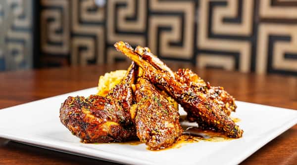 Grilled lamb chops with seasoning and a side of mashed potatoes on a white plate.