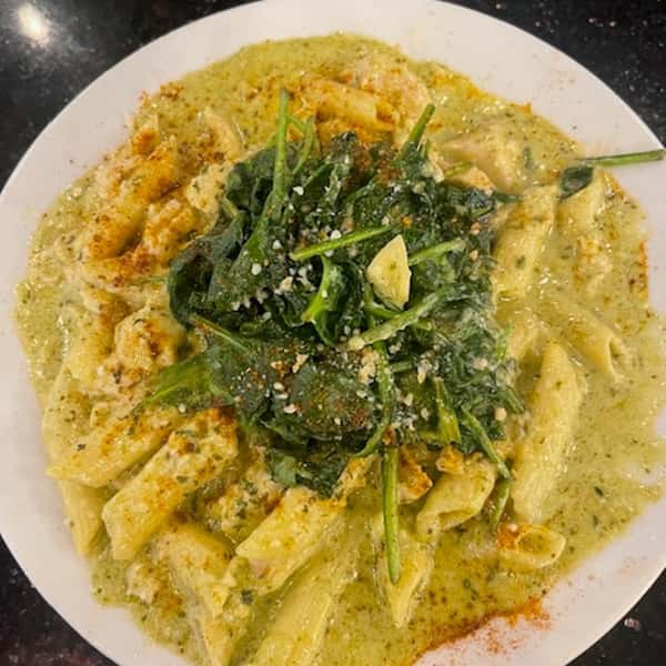 Penne pasta in a creamy pesto sauce, topped with sautéed spinach and sprinkled with grated parmesan cheese.