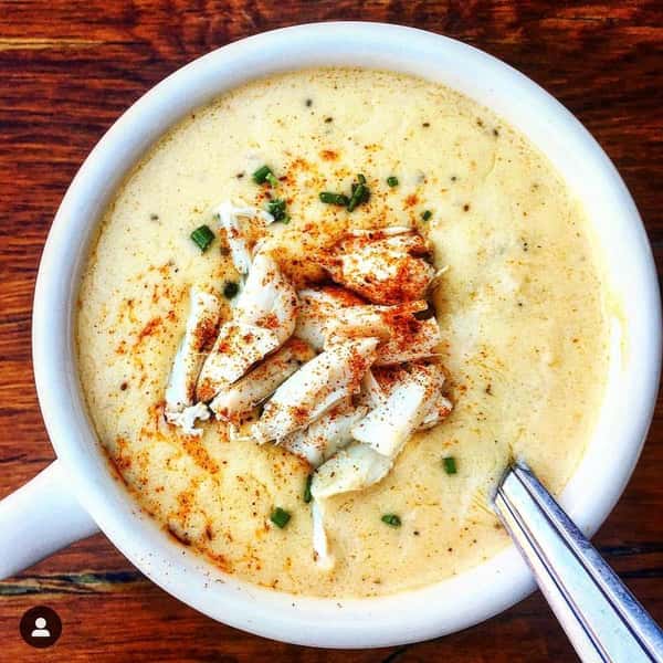 Creamy crab soup in a white bowl, topped with lump crab meat, chives, and a sprinkle of paprika.