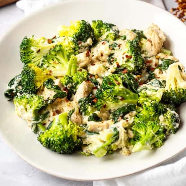Creamy chicken and broccoli skillet with spinach, topped with red pepper flakes, served on a white plate.