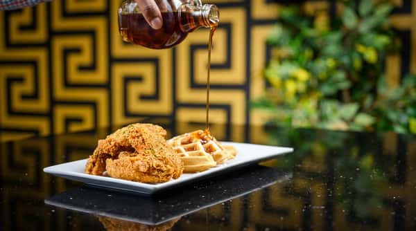 Fried chicken and waffles on a white rectangular plate, with syrup pouring from above.