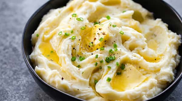 Creamy mashed potatoes with melted butter, fresh chives, and black pepper in a black bowl.