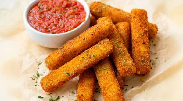 Mozzarella sticks with a side of red marinara sauce, garnished with herbs.