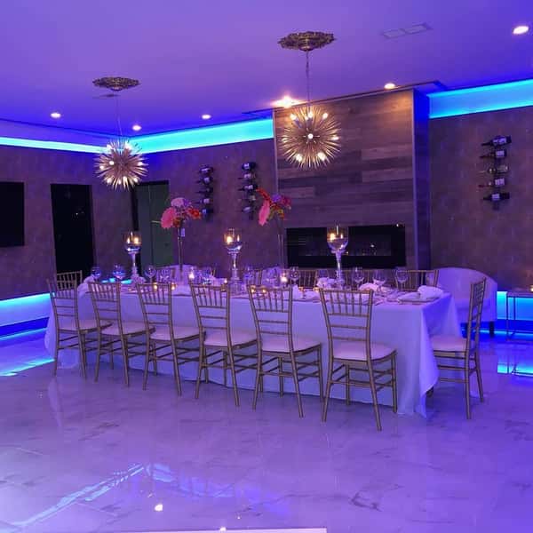 Elegant private dining room with gold chairs, modern lighting, floral centerpieces, and blue LED accents creating a luxurious ambiance.